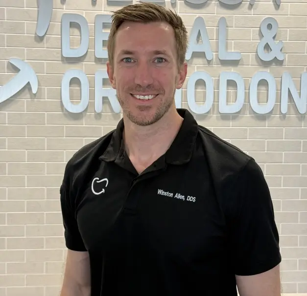 Dr. Winston Allen, DDS, smiling in front of dental practice signage in Dallas.